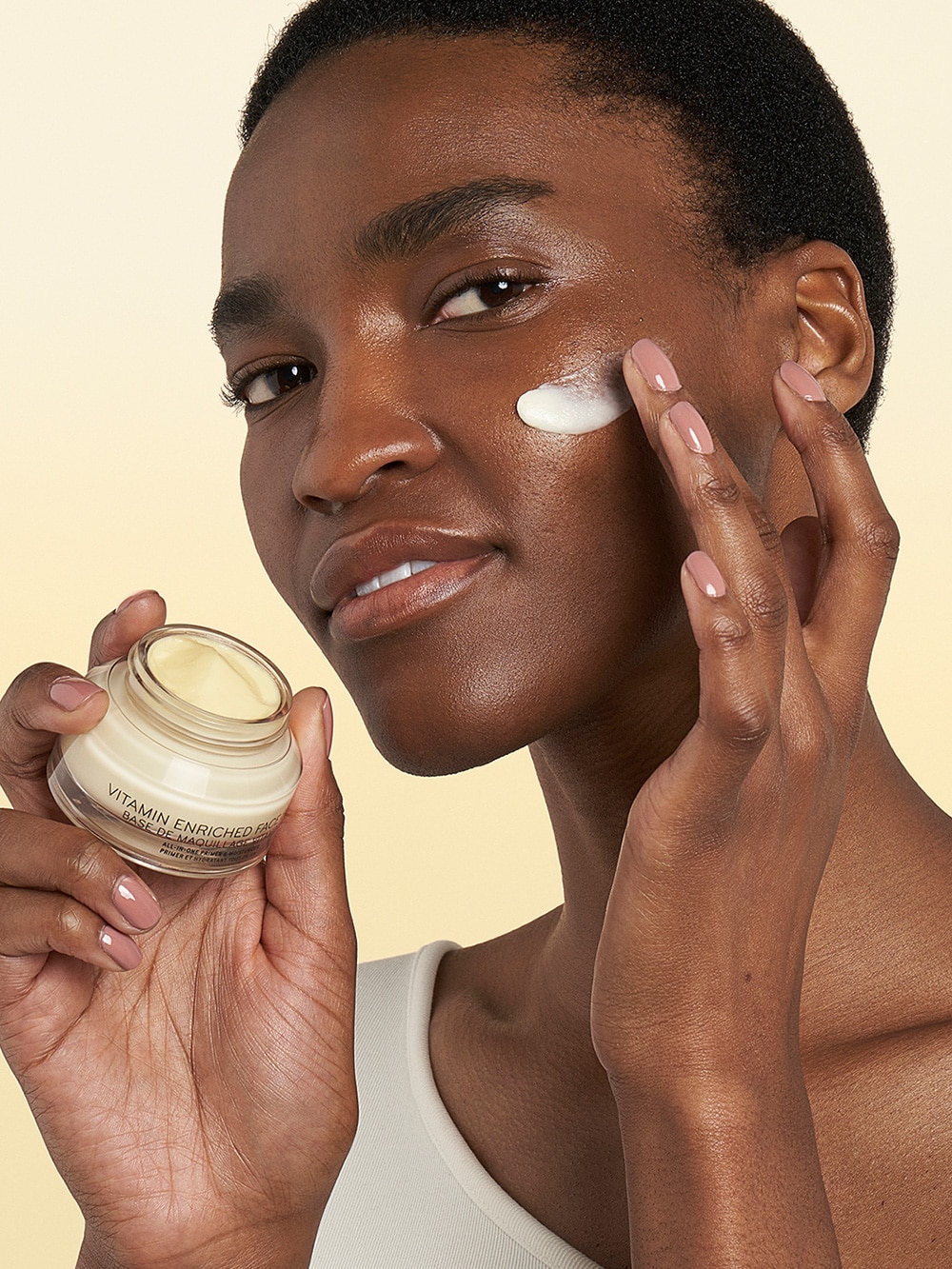 Model applying Vitamin Enriched Face Base to skin, focusing on the texture of the cream