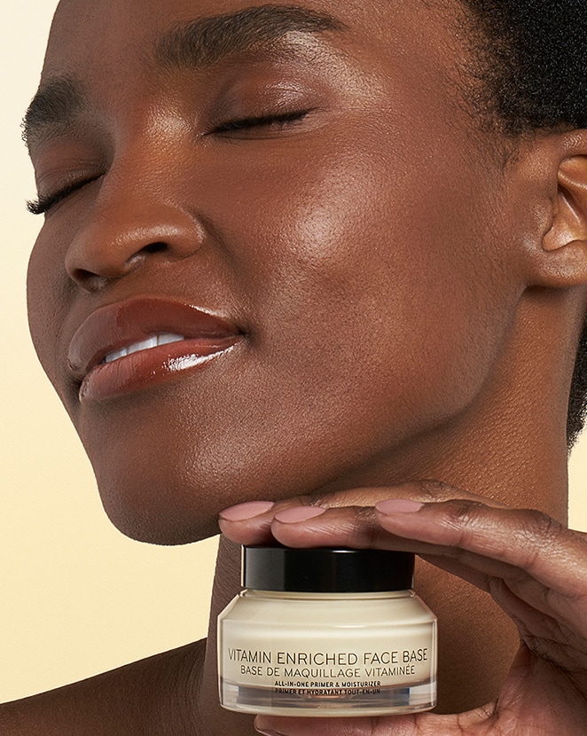 Model holding Vitamin Enriched Face Base, showcasing product application and an effortless glowing complexion